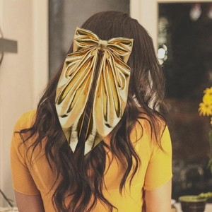 Elegant gold bow hair clip with metallic finish on model's long dark hair