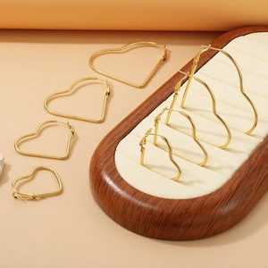 Golden heart-shaped hoop earrings in four different sizes displayed on a wooden stand
