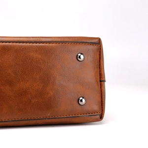 Brown textured PU leather tote bag showing protective metal bottom studs on base