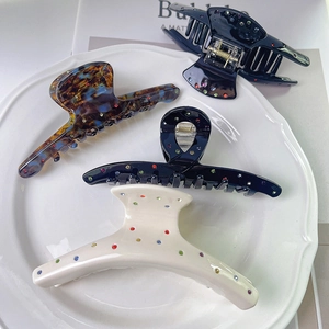 Detail of four acetate hair claws with colorful rhinestones on a white ceramic tray
