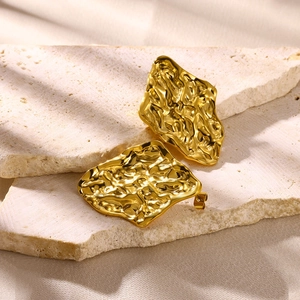 Macro detail of gold flower earrings with irregular wrinkled metal texture on stone