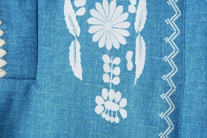 Detailansicht von jeansblauem Stoff mit weißen Gänseblümchen und geometrischen Drucken