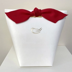 Close-up of white trapezoidal gift bag featuring a bright red ribbon bow and golden logo