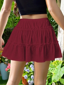 Detail view of burgundy tiered ruffle mini skirt with elastic waist in garden setting