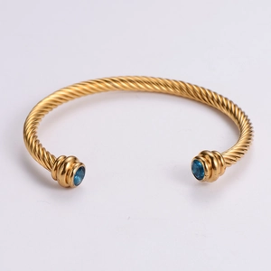 Bracelet torsadé doré avec pierres précieuses bleues aux extrémités sur fond épuré