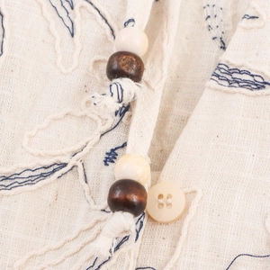 Women's V-neck blouse in beige linen fabric with blue embroidery and tassel wood bead details