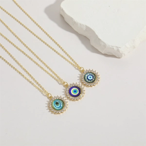 Three gold evil eye pendant necklaces with colorful resin and zircon accents on white background