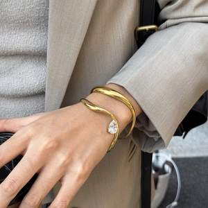 Nahaufnahme von goldfarbenem Wellenarmreif mit Zirkonia-Tropfen am Handgelenk einer Frau