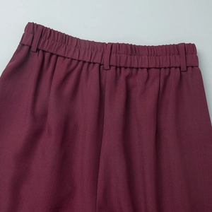Detail view of burgundy trousers featuring elastic waistband and fine fabric texture