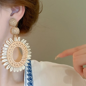Détail de boucles d'oreilles bohèmes en raphia tressé main style tournesol sur modèle