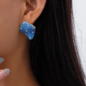 Close-up of blue geometric square earring with white dots and gold trim on model