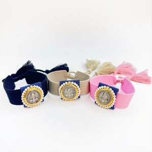 Handmade woven Saint Benedict medal bracelets with tassels in navy, beige, and pink