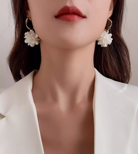 Detail of floral earrings with white petals and gold hooks worn with a white blazer