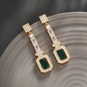 Macro view of gold-plated drop earrings with emerald green crystals and white zircons