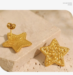 Detailed view of gold star earrings with unique hammered texture on a stone surface