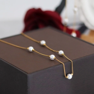 Elegant gold choker necklace with five white round pearls draped on a jewelry box