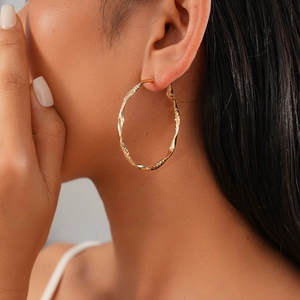 Macro detail of large gold twisted hoop earrings with textured finish on a model