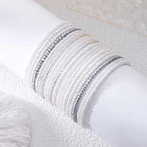 Detail of layered white and silver seed bead bracelet set on a nautical shell background
