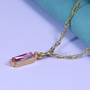 Macro shot of rectangular pink gemstone pendant set in gold on a fine wave chain