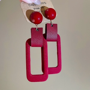 Detail showing red rectangular earrings with faux leather texture and metallic sphere studs