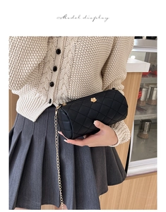 Close-up of black quilted cylinder bag featuring a gold flower buckle and chain strap