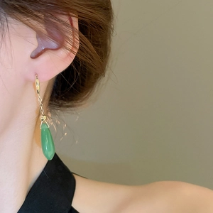 Detailed view of gold earrings with green teardrop stones on a professional model