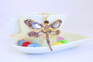 Detail of dragonfly keychain with purple crystals on a white heart cup edge