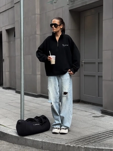 Detail of black oversized quarter-zip sweatshirt with 'tú eres' script and ripped jeans