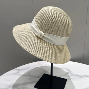 Detailed weave of beige straw sun hat with wide white ribbon and silver logo charm