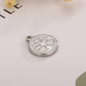 Detail of silver stainless steel round pendant with embossed Tree of Life pattern