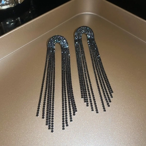 Macro shot of long dark tassel earrings with sparkling rhinestones on golden tray
