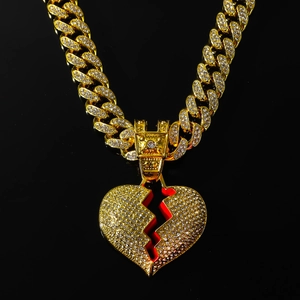 Close-up of golden iced-out Cuban chain with broken heart pendant and red enamel details