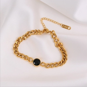 Chunky gold chain bracelet featuring a faceted black round stone on white satin fabric
