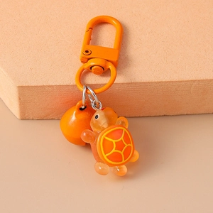 Close-up of orange turtle keychain with matching metal bell and hook on a beige background