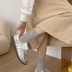 Detail of grey crew socks with pink bow embroidery paired with silver retro sneakers