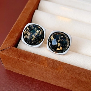Détail macro de boucles d'oreilles carrées avec gemme noire et feuilles d'or sur velours