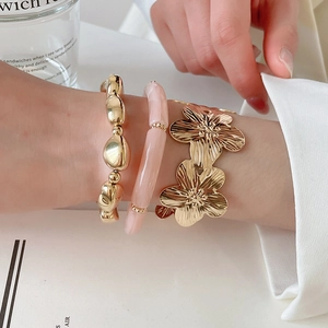 Dettaglio di un set di tre bracciali con fiori in metallo e perle di resina al polso.