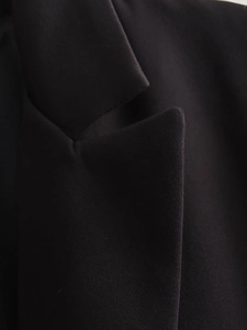 Detailed close-up of the notch lapel and fine weaving on a black tailored suit jacket