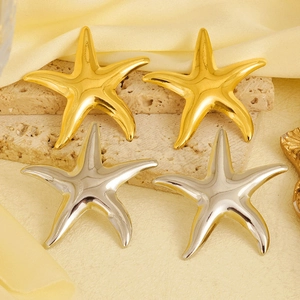 Macro detail of 18k gold and silver starfish earrings on a textured beige stone background