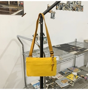 Detail of yellow nylon crossbody bag featuring front zipper pocket and adjustable strap