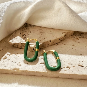Detailed close-up of U-shaped green enamel earrings on a marble stone surface