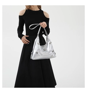 Detail of silver PU crossbody bag featuring metallic bow accents worn by a model