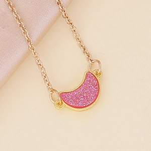 Golden moon necklace with pink glitter inlay on an elegant beige silk background