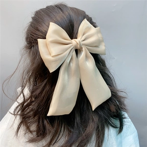 Close-up of elegant champagne satin bow hair clip with long ribbons on wavy hair