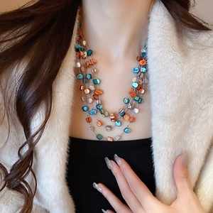 Close-up of layered necklace with irregular blue and orange shell beads on a model