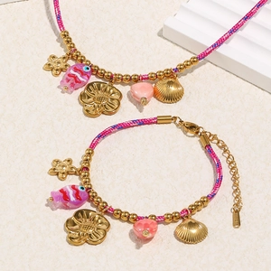 Détail de breloques coquillage et fleur plaquées or 18K sur cordon tressé rose