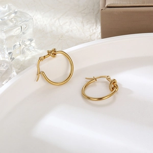 Elegant gold knot hoop earrings made of titanium steel displayed on a white textured surface