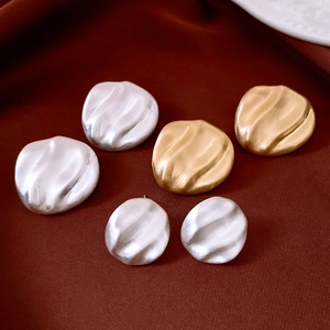 Macro view of six irregular wavy gold and silver stud earrings with matte brushed texture