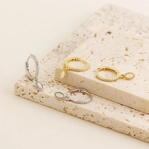 Detailed shot of gold and silver hoop earrings with teardrop opal charms on stone