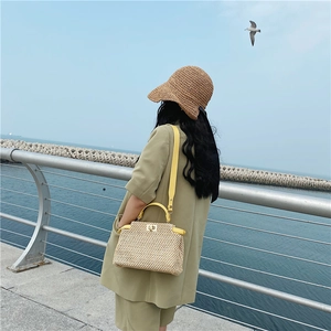 Outdoor lifestyle view of a woven straw shoulder bag with yellow leather trim at the beach